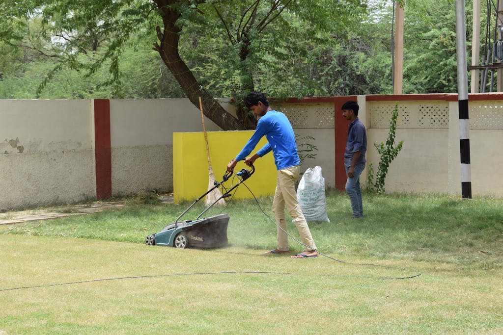 Young men working together on lawn maintenance with a mower in a sunny garden setting.